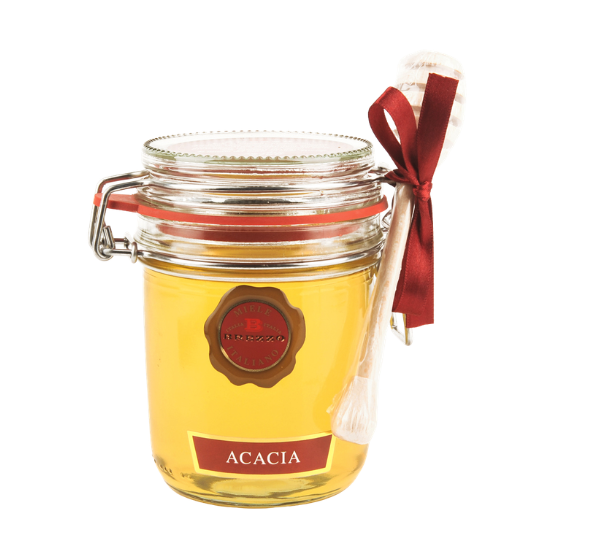 Jar of Acacia honey with a red seal, gold lid, and a honey dipper tied with a burgundy ribbon beside it